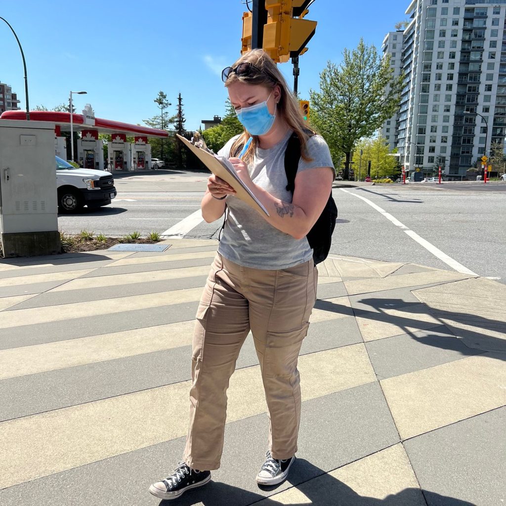 Research assistant wearing a mask, taking notes while surveying an intersection.