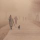 Individuals walking down a street on where there is smoke and haze in the air.