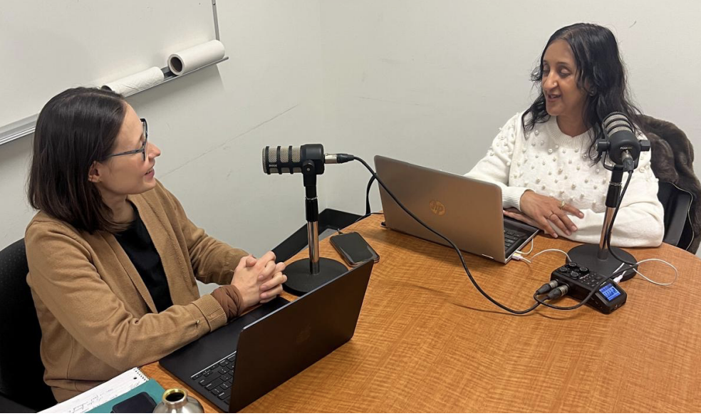Anu and Alfiya sitting at a table with computers and microphones, creating their podcast
